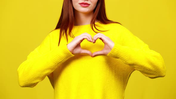 Unrecognizable Young Woman Making Heart Gesture Standing at Yellow Background Smiling