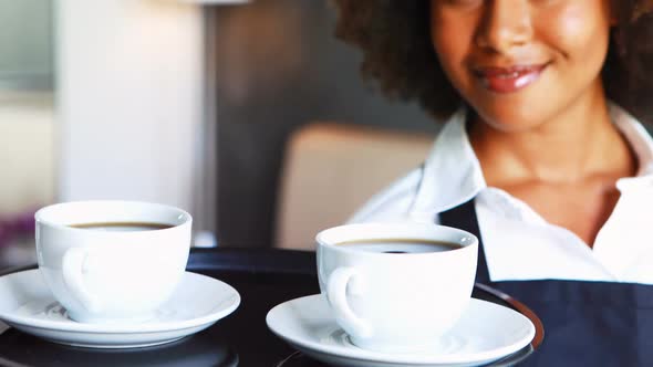 Portrait of smiling waitress holding tray of coffee cups