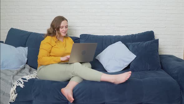 Woman is Sitting on the Sofa with Laptop and Typing Something