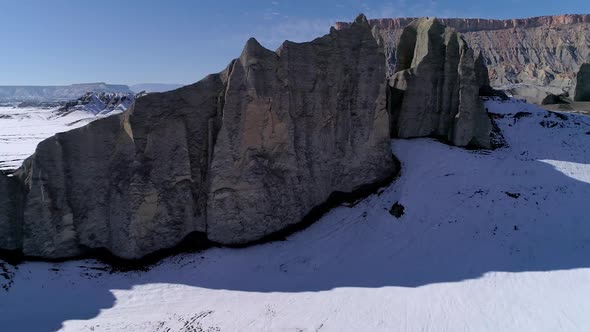 Flying towards and over rocky cliff viewing desert landscape in winter