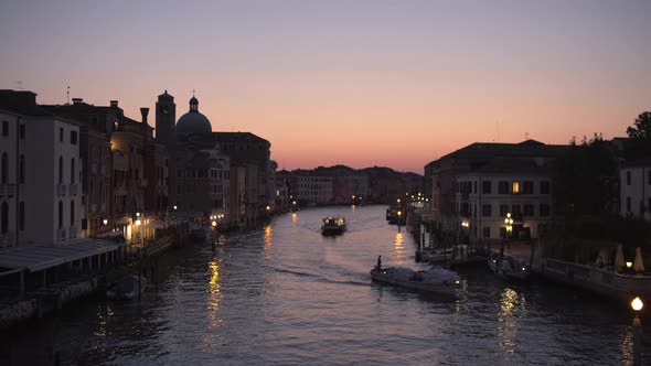 Wide static shot of boats cruising through Canal Grande at Twilight, Venice, Italy