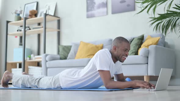 African Man Using Laptop on Yoga Mat at Home