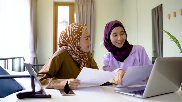 Two asian muslim women wearing hijab working together with using laptop pc tablet and paper chart