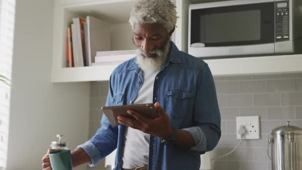 Video of happy african american senior man drinking coffee and using tablet