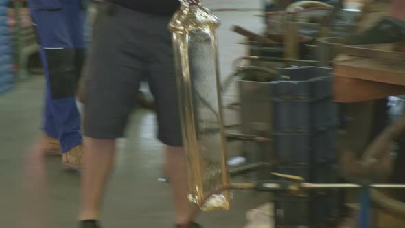 Worker Carries Bottle Walking Past Coworkers in Workshop