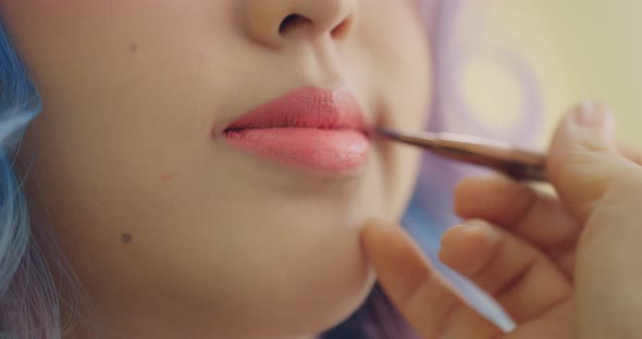 Close-up On Lips Of A Young Asian Woman. Makeup Artist Apply Lipstick To Model.