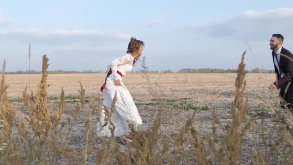 Happy Young Couple Holding Hands Run Through a Wide Field, Having Fun Outdoors