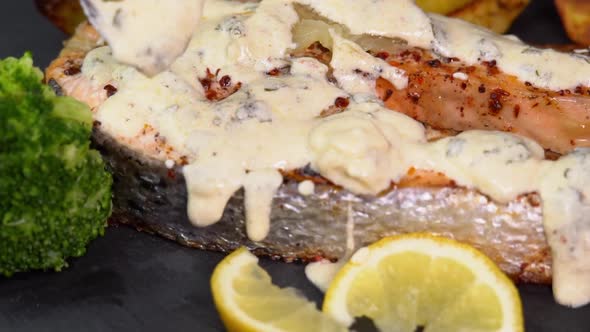 Grilled salmon steak pouring cream sauce and rotating on a black background with lemon slice