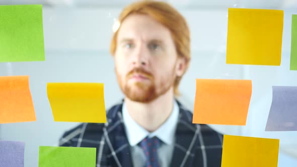 Redhead Businessman Working On Sticky Notes Attached on Glass