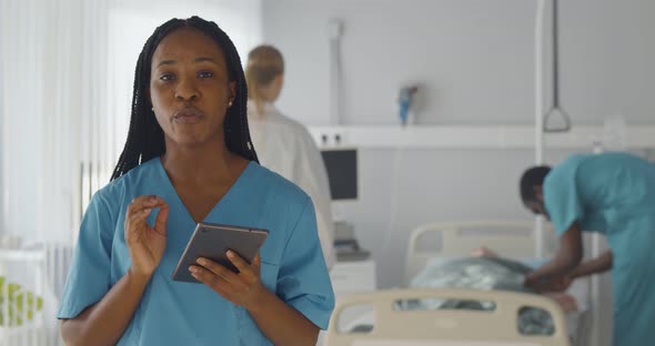 Afroamerican Woman Surgeon Holding Tablet and Talking at Camera