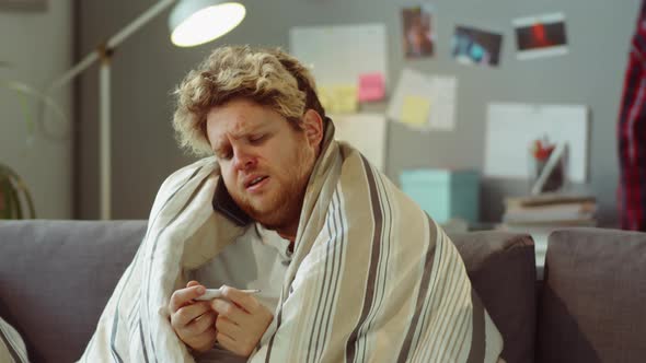 Sick Man Holding Thermometer and Calling Doctor at Home