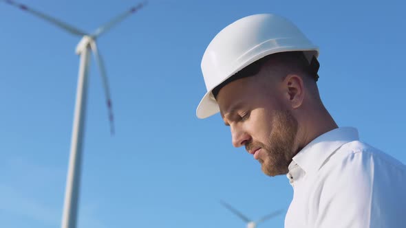 Portrait of a Man in a White Helmet and a Classic Shirt on the Background of a Wind Turbine of a