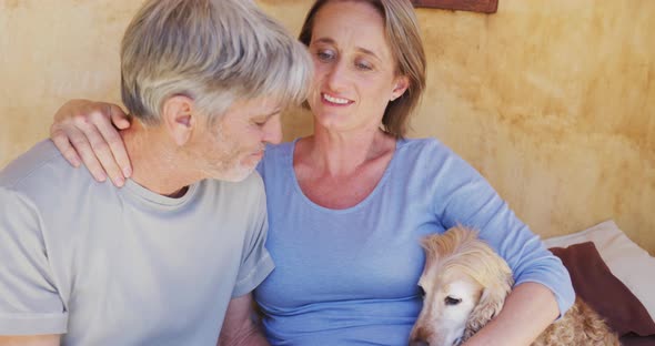 Smiling senior caucasian couple embracing and relaxing on porch with pet dog