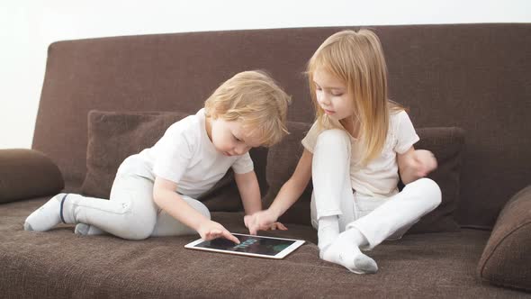 Little Caucasian Kids Use Tablet Sitting on Bed