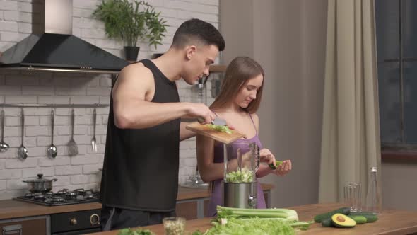 muscular young couple cooking healthy cocktail after workout, talking and laughing in the kitchen. 