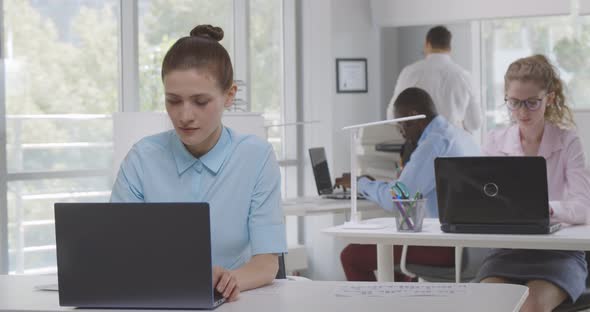 Portrait of Young Caucasian Businesswoman Working at Desk with Laptop in Busy Office