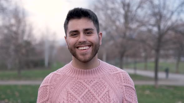 Hispanic Man looking at the camera and smiling while standing outdoors in the park.