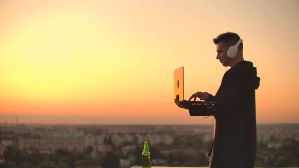 Hacker Using Laptop on Rooftop with City View and Forex Chart. Hacking and Stats Concept