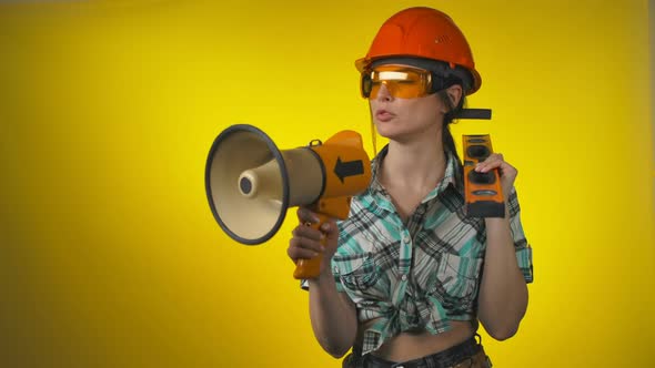 Female Builder in an Orange Safety Helmet is Shouting Through Megaphone