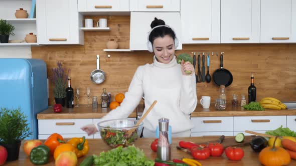 Young Cheerful Girl Singing In Broccoli Dancing In The Kitchen While Cooking Dinner.