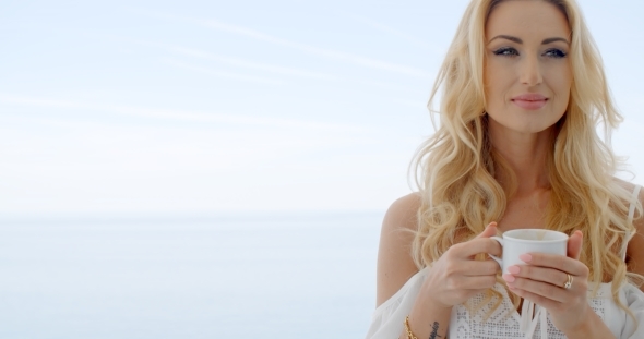 Blond Woman Holding Coffee Cup In Front Of Ocean