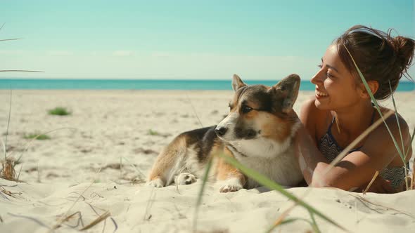 Happy Affectionate and Tender Tanned Woman in Bikini Lying on Sand at Sunny Sea Beach with Her Pet