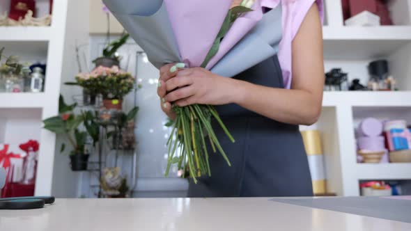 Florist is Packaging Bouquet From Roses and Leaves in Paper Closeup Hands