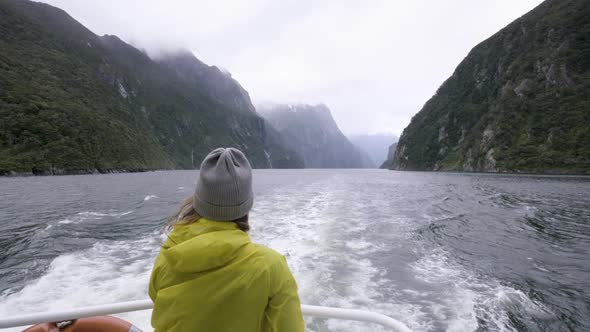Slow motion shot of girl in yellow rain jacket on back of boat surrounded by mountains and fiords. M