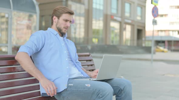 Man with Back Pain Using Laptop While Sitting Outdoor on Bench