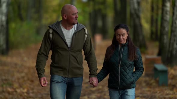 A Smiling Middle-aged Couple in Love, a Woman with Dark Hair and a Bald Man Walk Through the Autumn