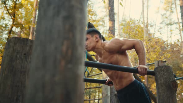 Muscular man doing push ups exercises on parallel bars. workout in the forest gym, outdoors.