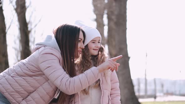 Young Pretty Mother Is Pointing at Something Hugging Her Daughter in a Park