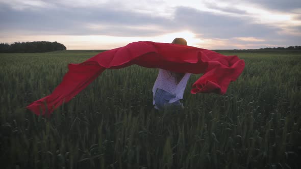 Young Girl Running with Red Tissue in Green Field. Happy Cute Girl Playing in the Wheat Field on a