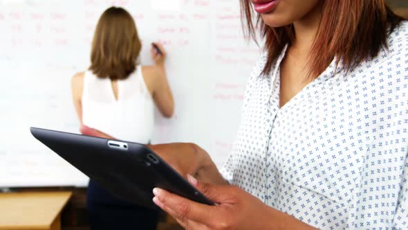 Business executive using digital tablet while colleague writing on white board