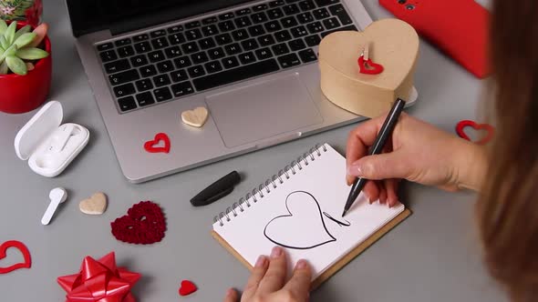 Young woman writing a card I LOVE YOU while wrapping valentine's day gift 