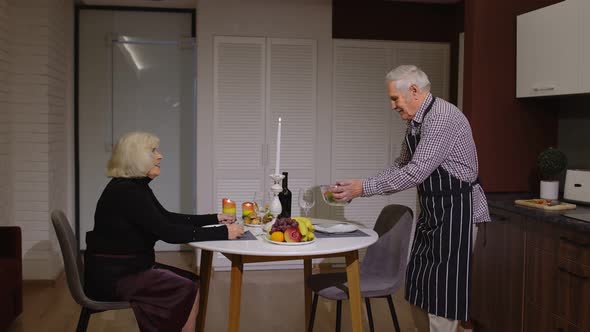 Old Elderly Man Cooking for His Wife a Romantic Supper with Wine and Candles. Senior Couple in Love