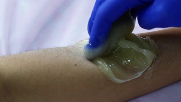 Depilation master woman applying sugar paste on the leg during the procedure of epilation