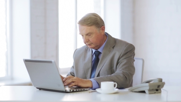 Senior Man With Laptop Drinking Coffee At Office