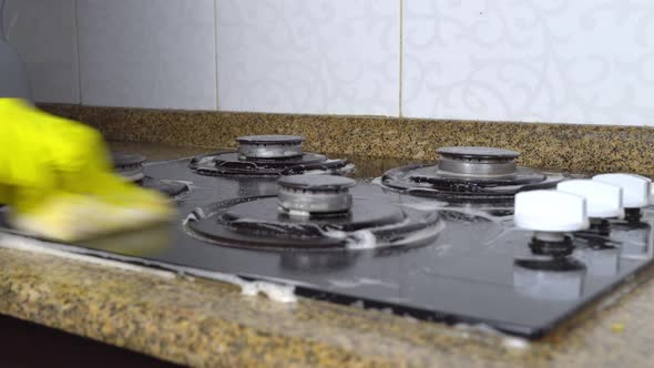 housewife woman in yellow gloves washes gas stove in kitchen with sponge.