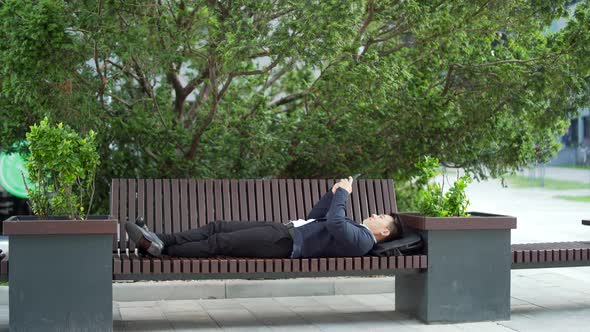 asian businessman office worker relaxes lying on a bench with a mobile phone in his hands.