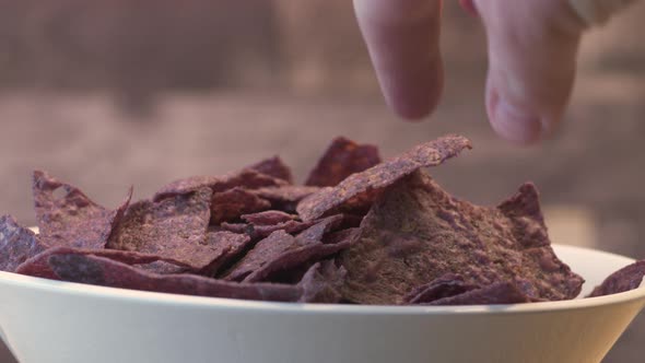 Hand grabbing a chip from a bowl of blue nachos.