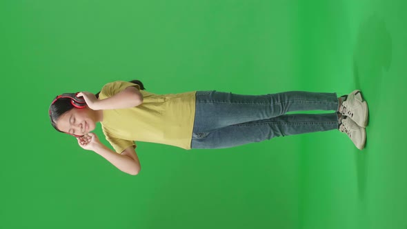 Full Body Of Young Asian Kid Girl Listening To Music With Headphones And Dancing In The Green Screen
