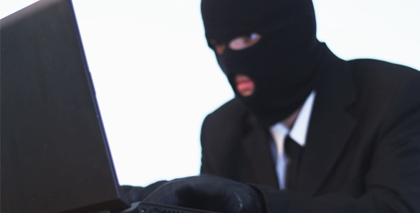 Hacker in a Mask and Gloves Hacking Laptop