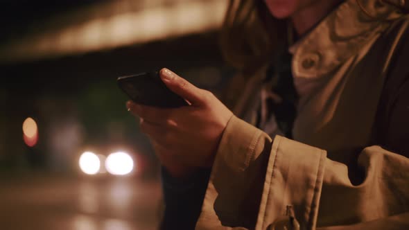 Female hands holding phone with blurry evening city lights in the background
