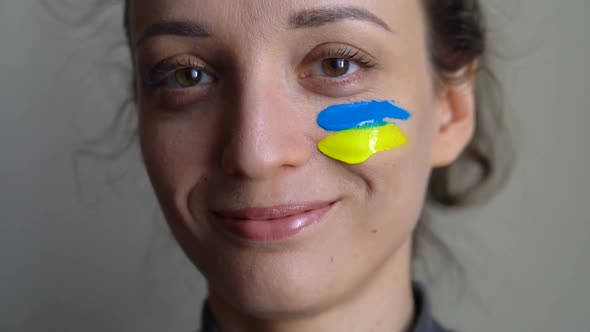 Indoor Portrait of Young Girl with Blue and Yellow Ukrainian Flag on Her Cheek Wearing Military