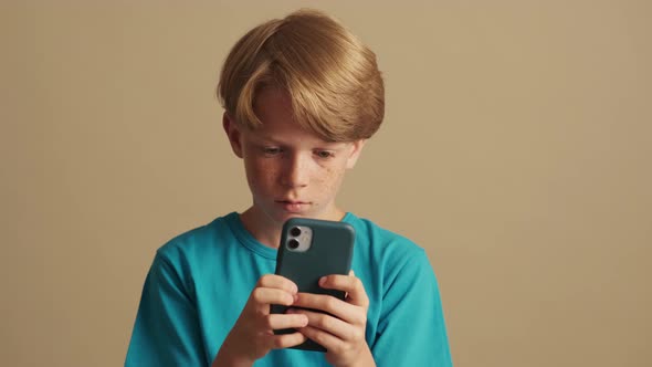 A concentrated little boy is using his mobile