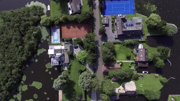 A topdown drone shot panning forward, over a small road with houses and water on either side, in the