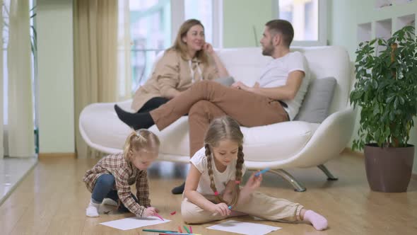 Wide Shot of Relaxed Happy Little Girls Drawing with Blurred Couple of Parents Sitting on Couch