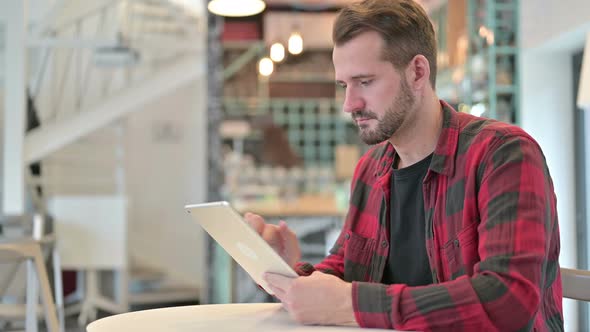 Serious Young Man Using Digital Tablet in Cafe 