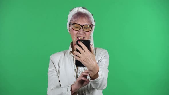 Portrait of Old Stylish Woman Is Talking for Video Chat Using Mobile Phoneisolated Over Green